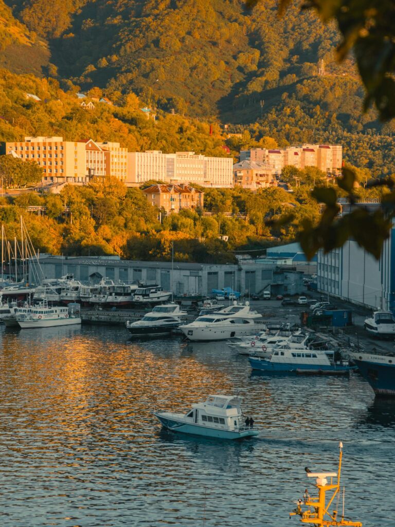 Picturesque harbor at sunset with yachts, buildings, and lush hills in the background.